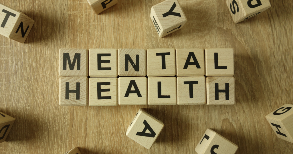 Wooden letter blocks spell 'MENTAL HEALTH' on a wooden table with other blocks scattered around.