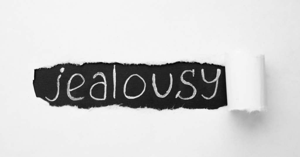 Torn black paper strip with the word jealousy written in white chalk on a white background edge on the right.