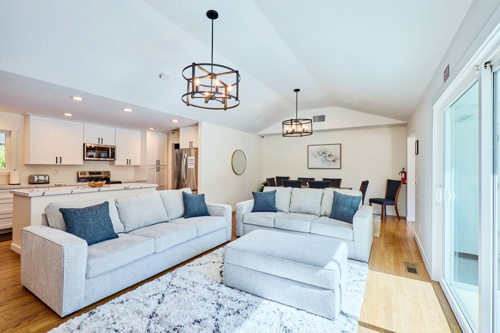 Open-concept living area with two gray sofas, a white kitchen island, and a dining nook in the background.